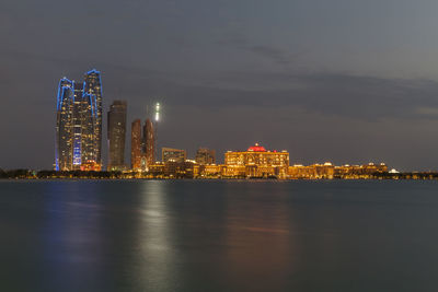 Illuminated buildings by sea against sky at night