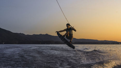 Latino mas doing wakeboarding in a lake with mountains in the background