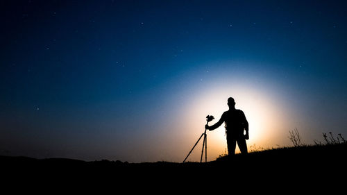 Silhouette man photographing against sky at night