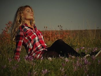Woman sitting on field against sky
