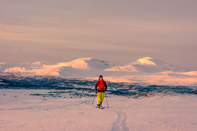 Rear view of man standing on snowy mountain against sky during sunset