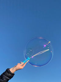 Hand holding bubbles against clear blue sky