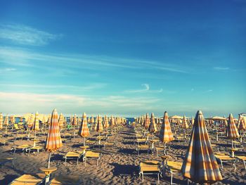 Parasol and empty lounge chairs on sand at beach against sky
