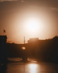 Silhouette buildings by river against sky during sunset