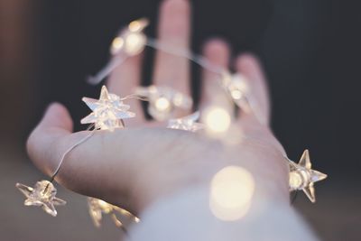 Cropped hand of woman holding illuminated string lights