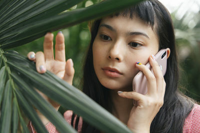 Close-up of young woman talking on phone by plant