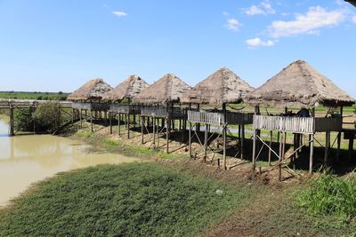 Stilt houses by trees against sky