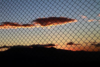 Close-up of chainlink fence against sky during sunset