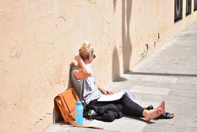 Young woman sitting against wall