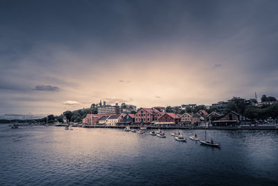 Scenic view of river by buildings against sky at sunset