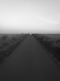 Street amidst grassy field against sky