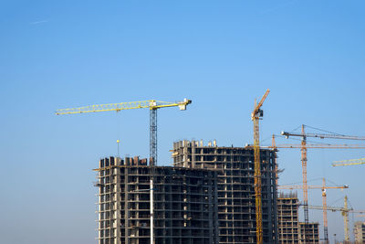 Low angle view of crane by building against clear blue sky