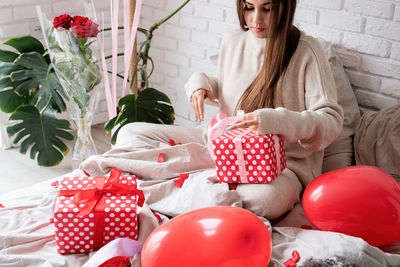 Young caucasian brunette woman sitting in the bed celebrating valentine day wrapping the gifts