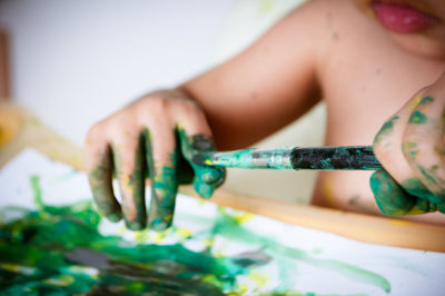 Midsection of child holding paintbrush with watercolor paints