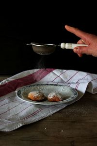 Hand sprinkling powdered sugar over cookies in plate