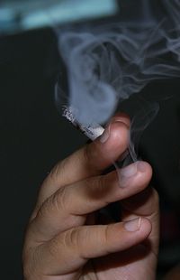 Close-up of hand holding cigarette with smoke in darkroom