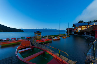 Boats moored in sea by houses against blue sky