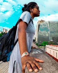 Side view of young woman standing against sky in city