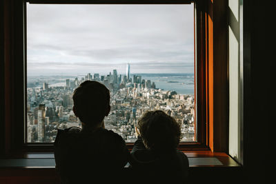 Rear view of brothers looking at cityscape through window at home