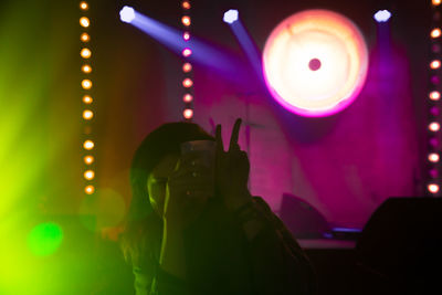 Woman gesturing while holding drink at illuminated nightclub