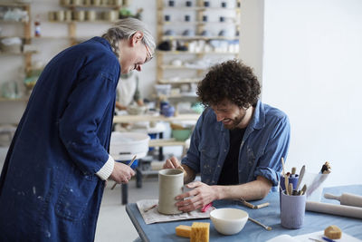 Smiling male and female students learning pottery in art studio