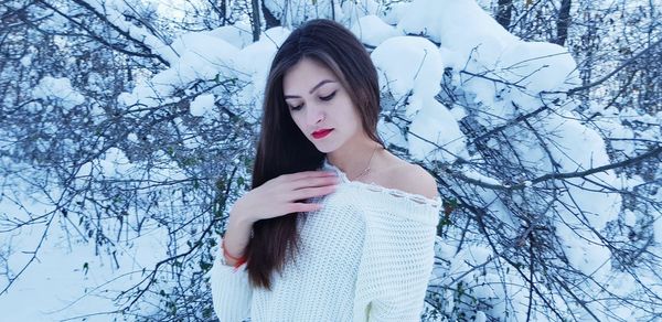 Beautiful young woman standing against snow covered bare tree in forest