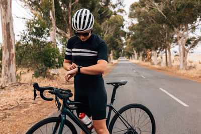 Cyclist checking watch while standing on road