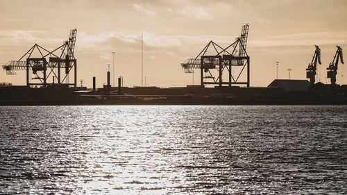 Silhouette cranes at commercial dock against sky during sunset