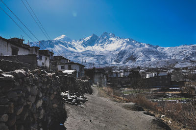 Snow covered buildings by mountain against blue sky