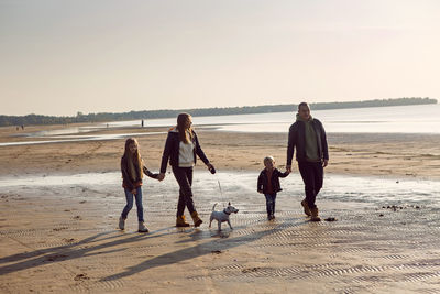 Rear view of people walking at beach against sky