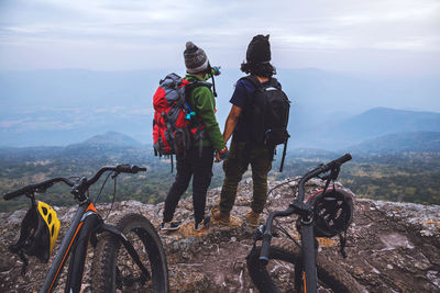 Rear view of people with bicycles standing on mountain against sky