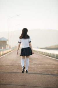 Rear view of woman wearing uniform while walking on road against sky