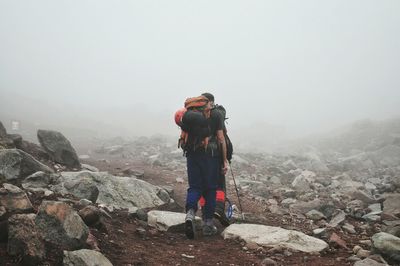 Rear view of hiker with friend on mountain during foggy weather