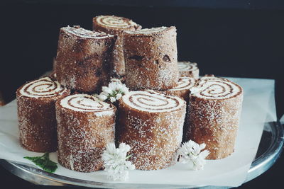 Swiss rolls decorated with flowers in plate against black background