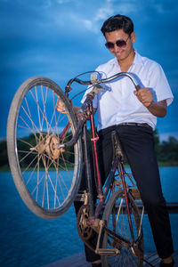 Teenage boy riding bicycle by lake at dusk