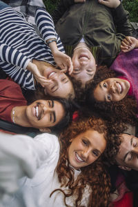 Directly above view of cheerful teenage friends lying down at park