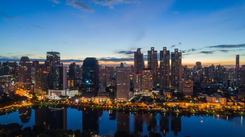 Illuminated buildings by river against sky in city