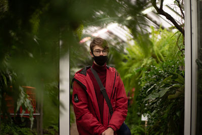 Portrait of teenage boy wearing mask standing against plants