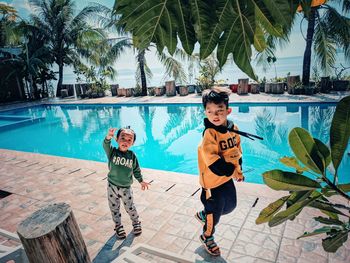 Full length portrait of boys standing by swimming pool against trees