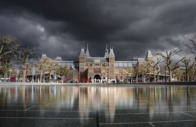 Buildings by river against cloudy sky