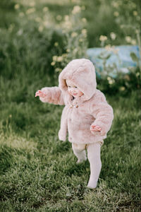 Baby girl first steps in pink fur coat outside on grass