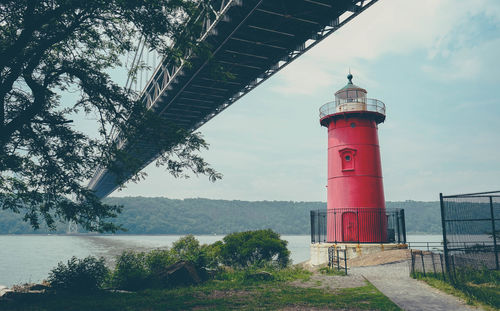 Lighthouse by bridge over river against sky