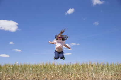 Full length of woman jumping on field against blue sky