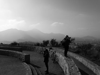 Rear view of people standing on mountain against sky