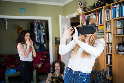 Blond girl wearing virtual reality headset by friends at home