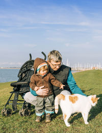 Grandfather and granddaughter with cat on grassy field