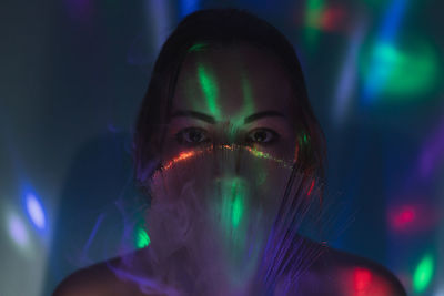 Close-up portrait of young woman holding multi colored fiber optic and smoke