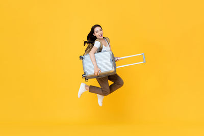 Portrait of young woman jumping against yellow background