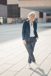 Smiling business person standing with hand in pocket at office park on sunny day