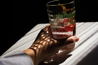 White female american hand holding glass of water on minimal white and black background, closeup